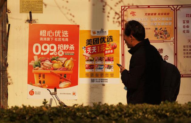 12月9日，天津和平区一小区外，市民从几家社区电商的海报前走过 视觉中国图